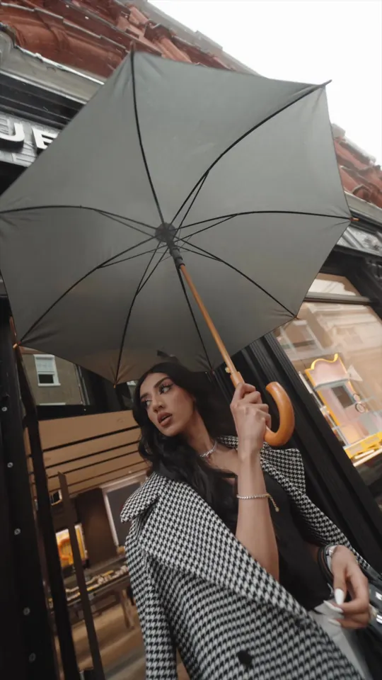 Tam Kaur under a grey umbrella outside the Hublot boutique in London, wearing a houndstooth coat