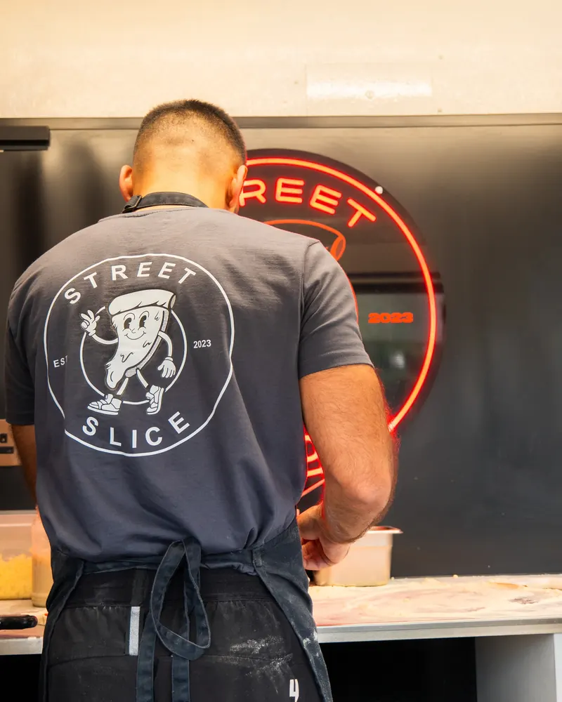 A Street Slice chef in a branded shirt under the neon sign