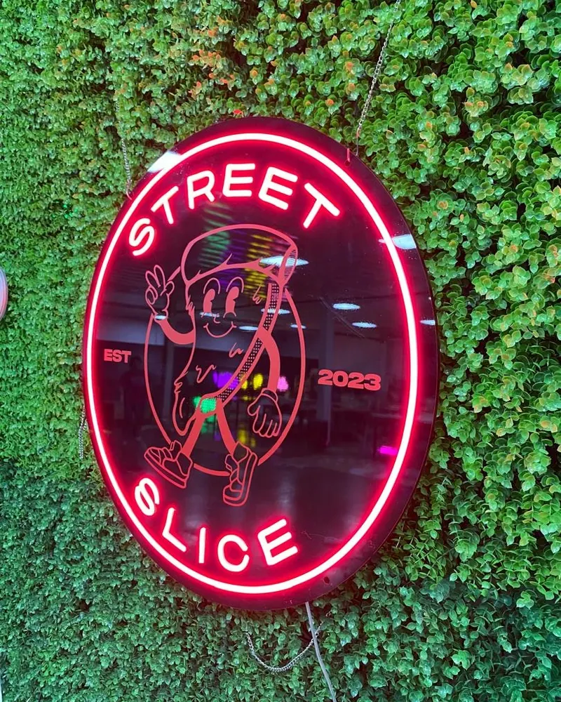 Round neon Street Slice sign mounted on a green foliage wall