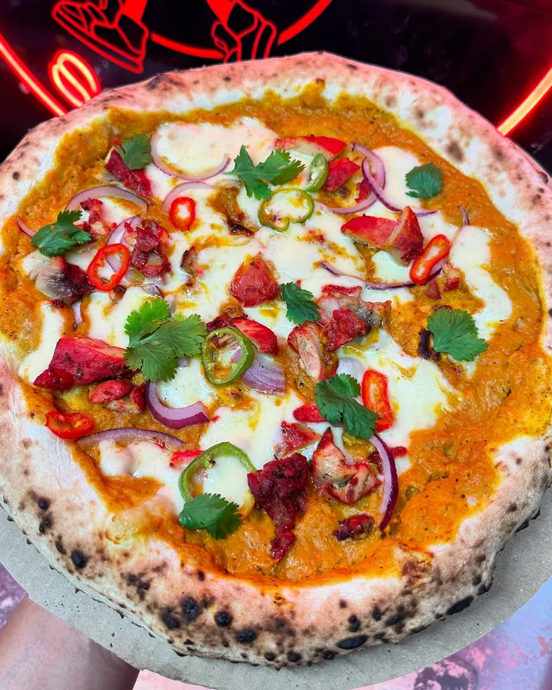 A Street Slice pizza held up in front of red neon lighting